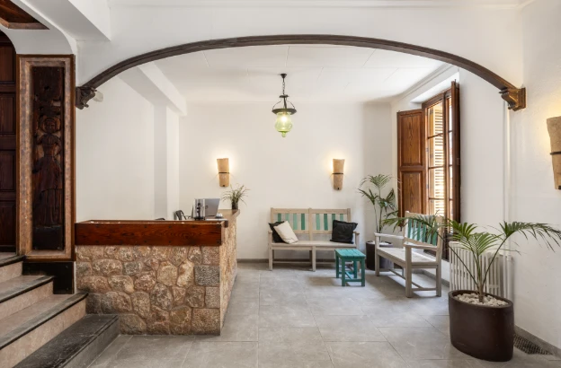 Recepción interior con mostrador de piedra, bancos y plantas decorativas.