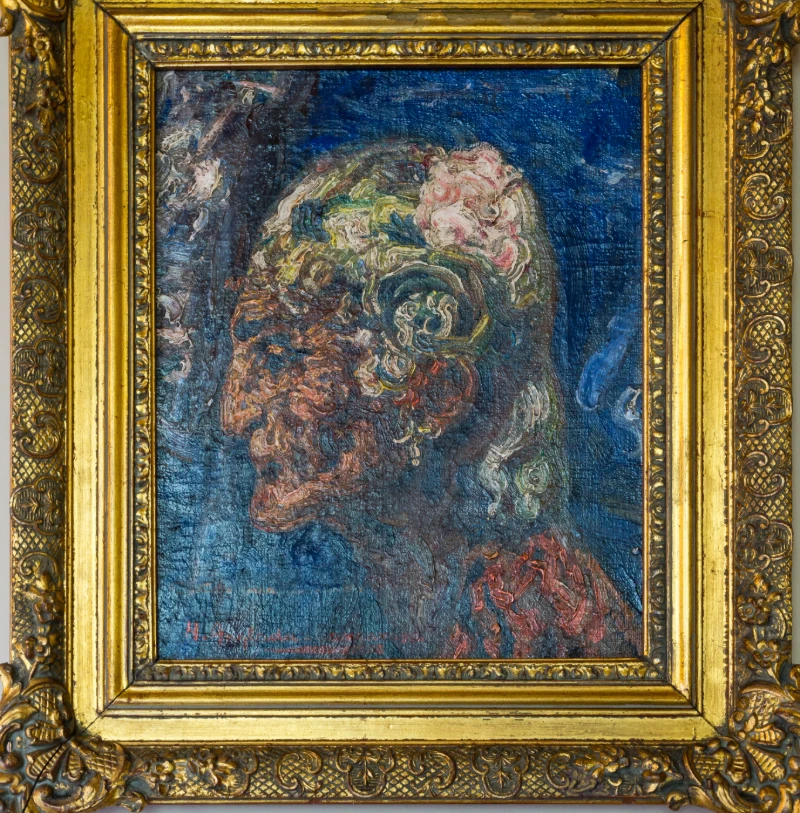 Pintura al &oacute;leo de un rostro con flores en un cuadro dorado.