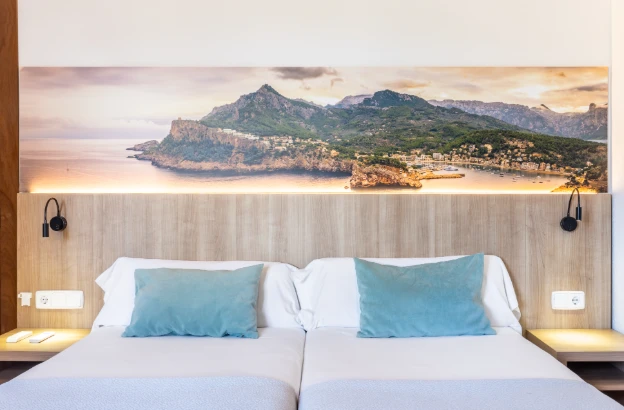 Cama en un hotel con vista al mar y montañas al fondo.