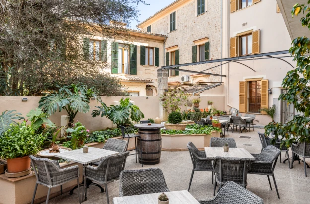 Patio soleado con mesas y sillas y plantas alrededor de una casa italiana