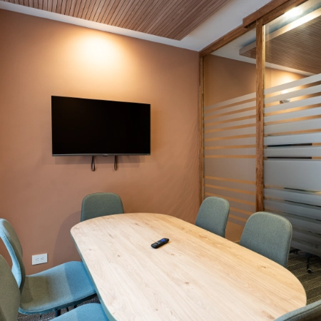 Sala de reuniones con mesa de madera, sillas azules y TV en pared