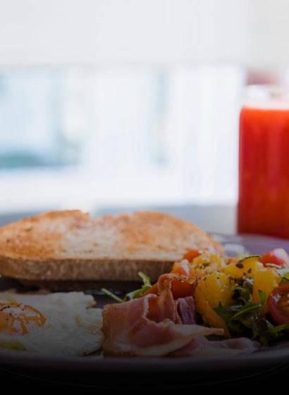 Rebanada de pan con jam&oacute;n, verduras y huevo sobre plato, fondo desenfocado.