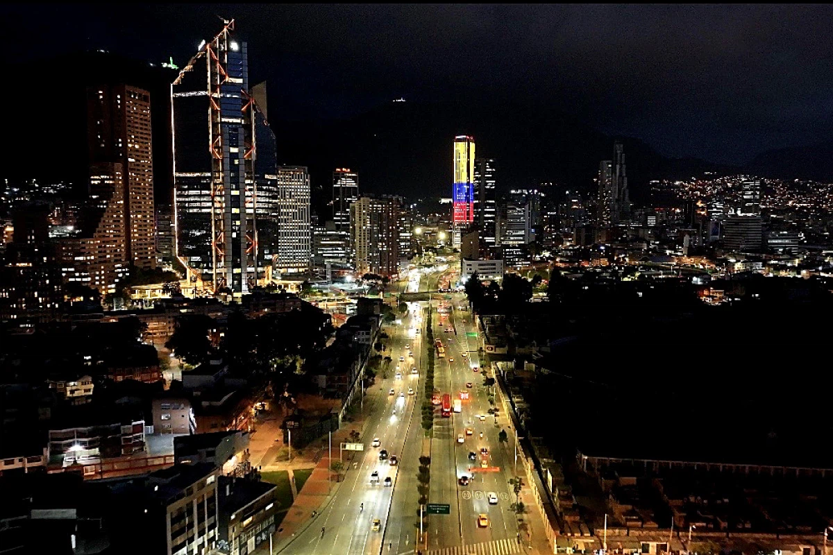 Vista nocturna de una avenida con rascacielos iluminados y tr&aacute;fico.