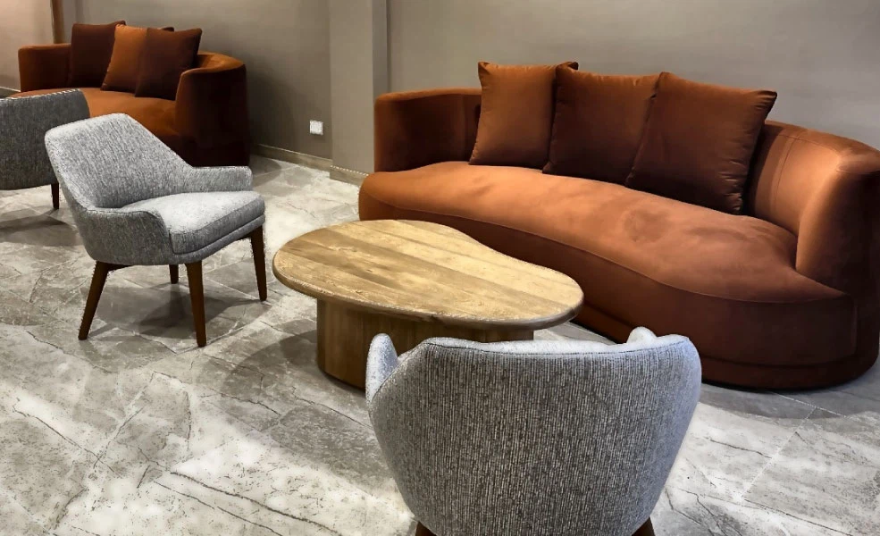 Sala moderna con sof&aacute; marr&oacute;n, sill&oacute;n gris y mesa ovalada de madera.