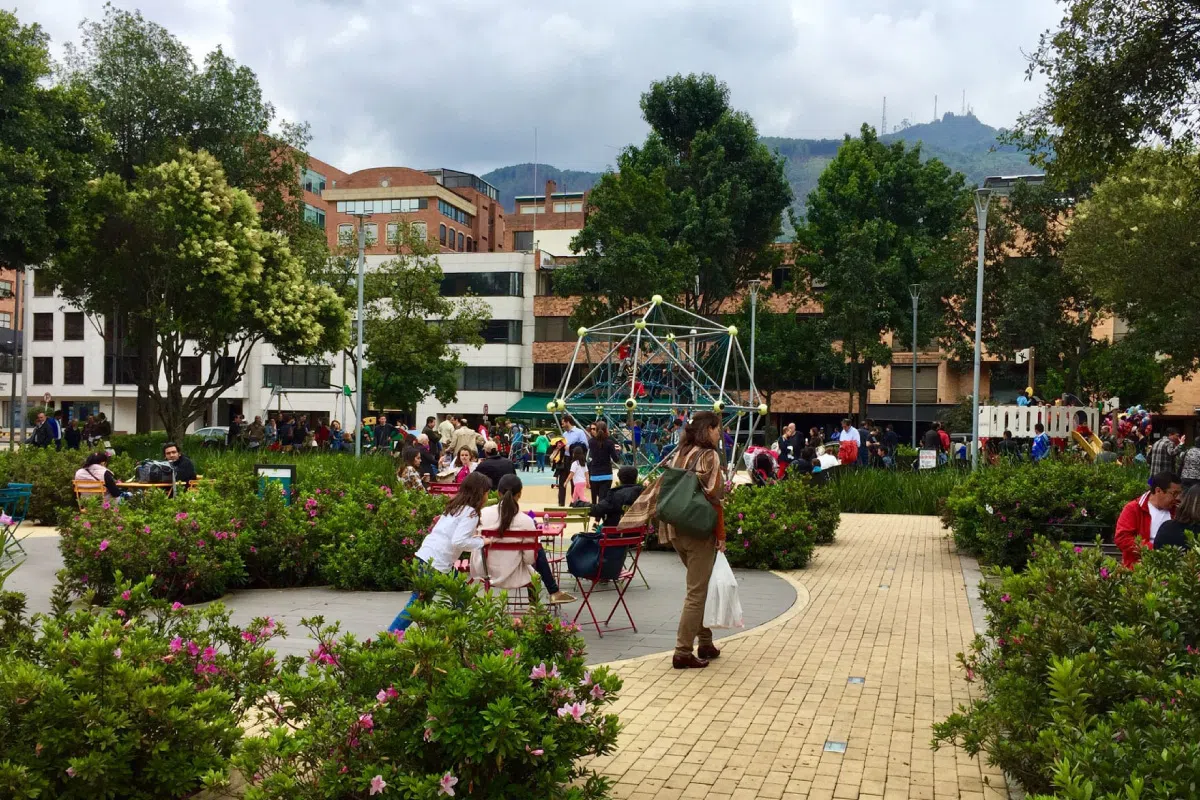 Parque con jardines, gente y columpio de malla en campus universitario.