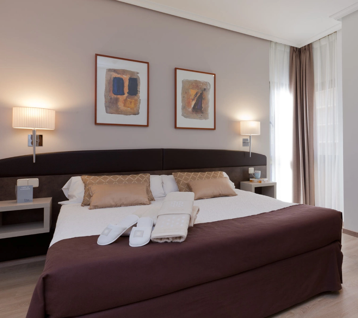 Dormitorio moderno con cama, almohadas, l&aacute;mparas y cortinas junto a ventanas