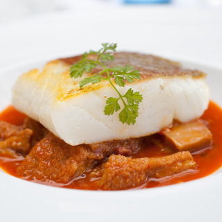 Medall&oacute;n de pescado con salsa roja y guarnici&oacute;n de hierbas frescas