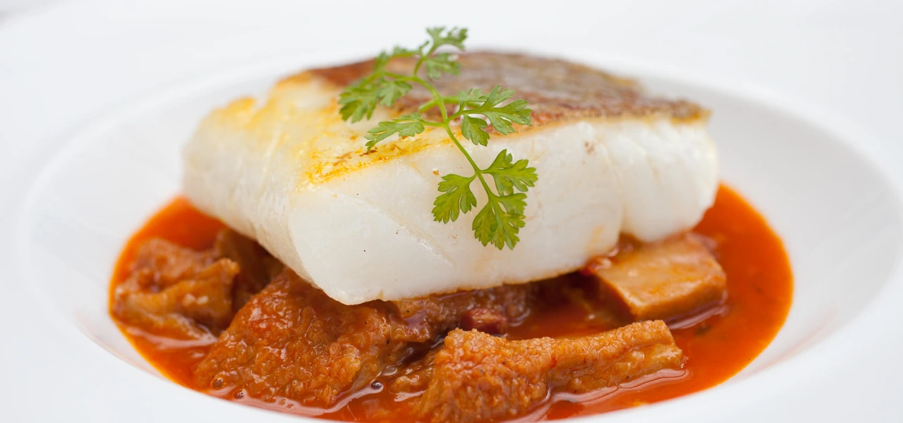 Lomo de bacalao sobre estofado con salsa roja y perejil fresco.