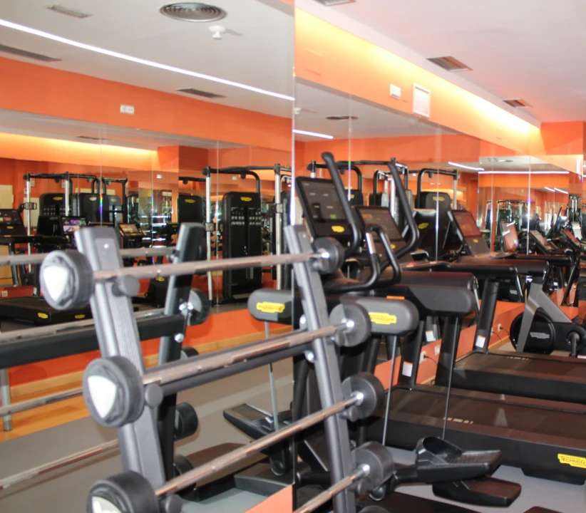 Gimnasio con m&aacute;quinas de ejercicio y pesas en sala amplia y luminosa.