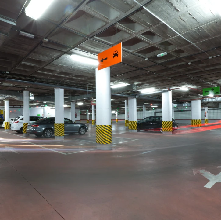 Aparcamiento subterr&aacute;neo con coches, columnas blancas y flecha naranja.