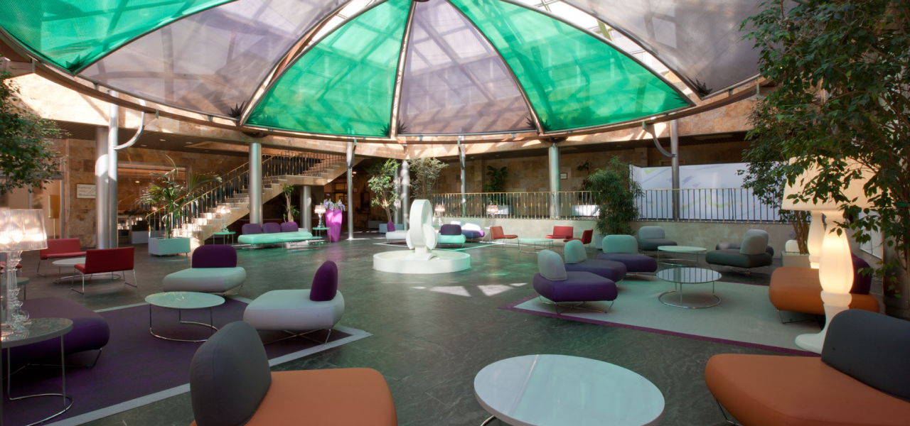 Patio interior con sof&aacute;s modernos, mesas y toldo verde transl&uacute;cido.