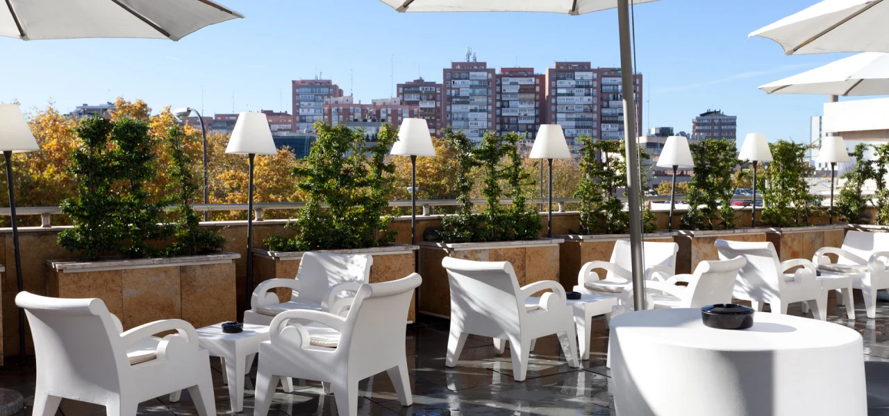 Terraza urbana con mesas y sillas blancas bajo sombrillas, vista a edificios