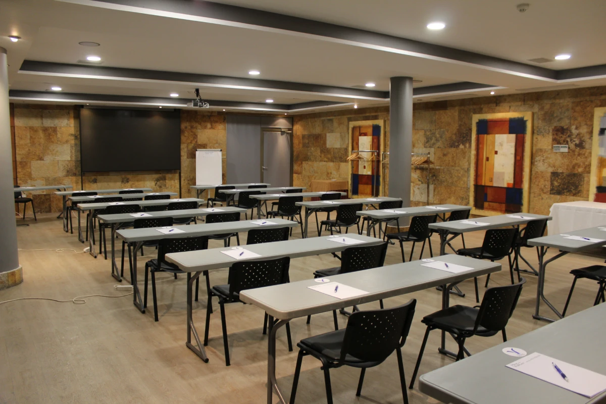 Aula con mesas y sillas, pizarras y paneles de madera, luces de techo encendidas.