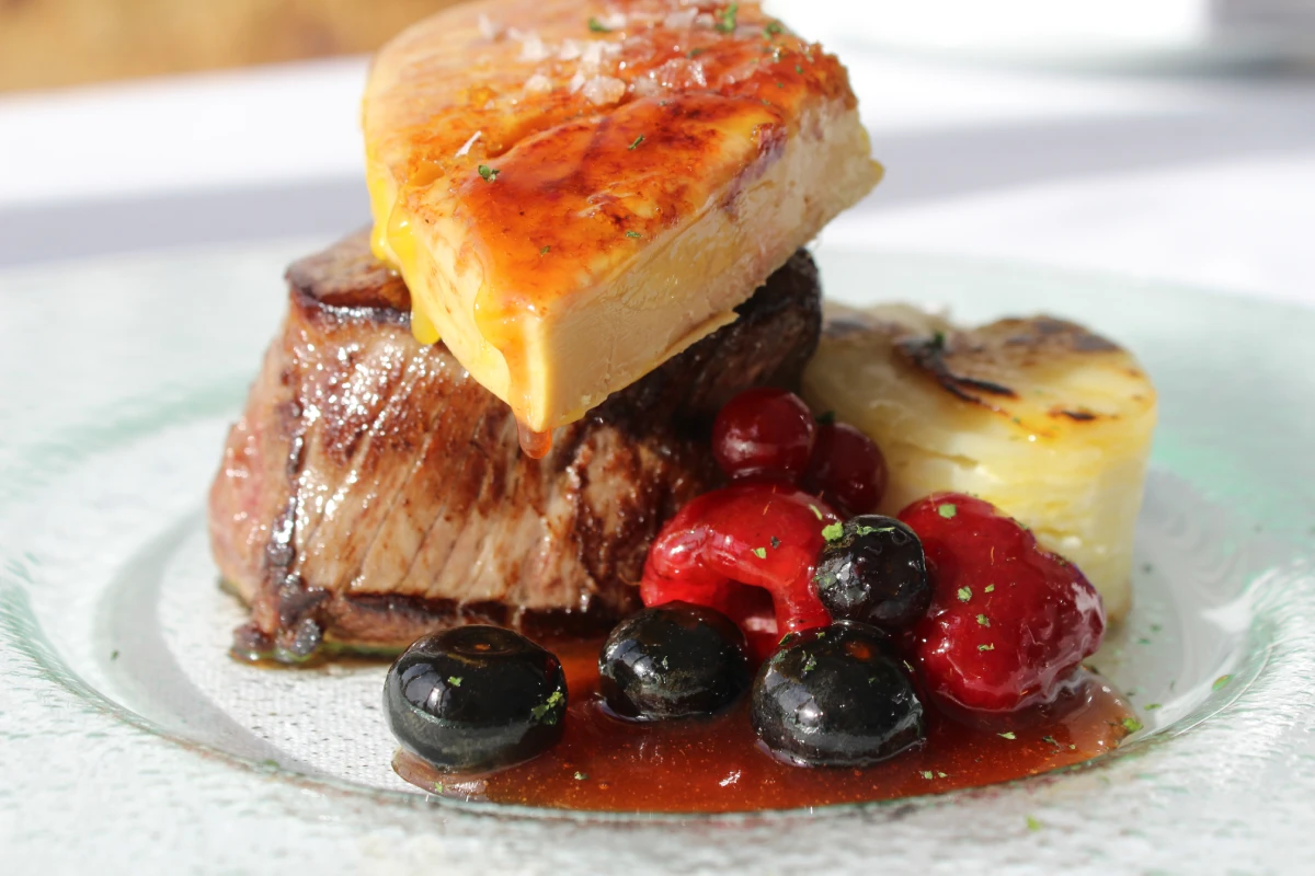 Filete con queso derretido y aceitunas negras, guindas y verduras en plato