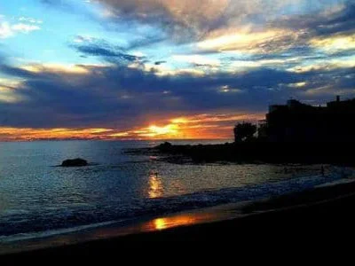 Atardecer en la costa con cielo nublado y silueta de &aacute;rboles y playa