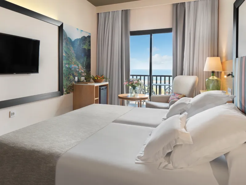 Habitaci&oacute;n de hotel moderna con cama, l&aacute;mpara y vista al mar por ventana