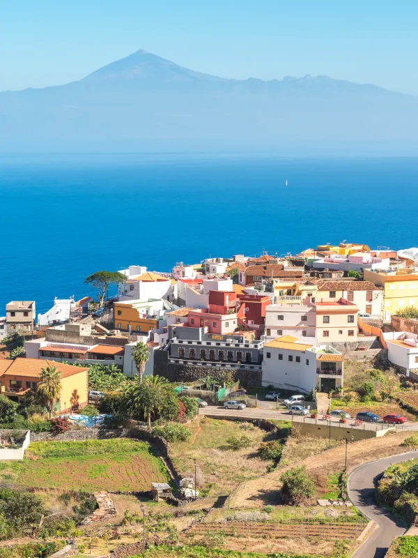 Pueblo costero con casas de colores y el volc&aacute;n al fondo sobre el mar