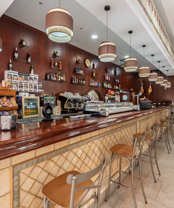 Interior de una cafeter&iacute;a con barra de madera, estanter&iacute;as y sillas altas