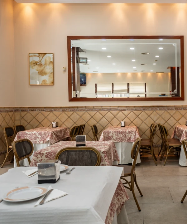 Comedor de restaurante con mesas cubiertas y sillas, luz c&aacute;lida interior.