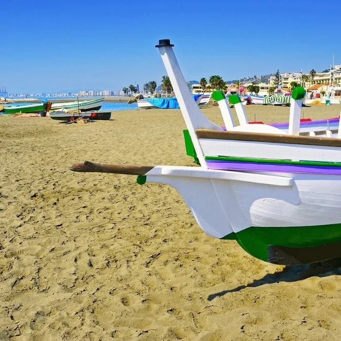 Barcas de colores en la playa, cielo azul y arena.