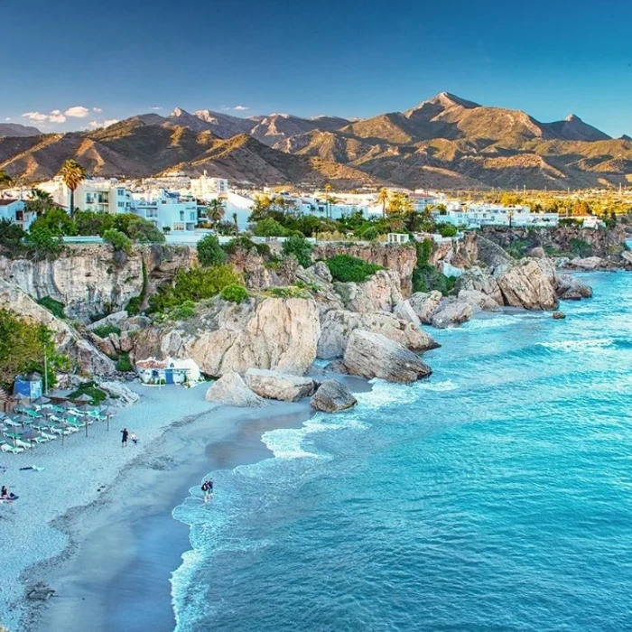 Playa azul con acantilados, palmeras y montañas al fondo.