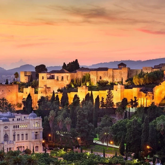 Jardines y murallas iluminadas de un palacio al atardecer con cielo rosado