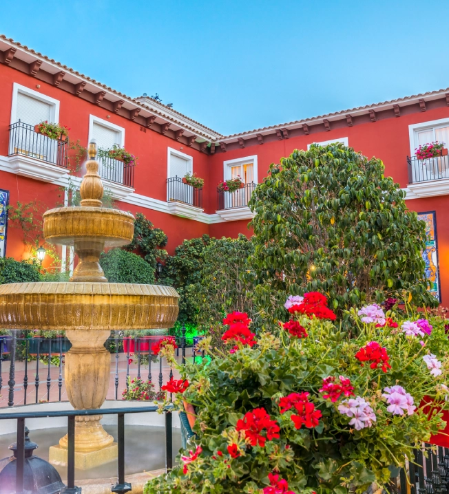 Fuente de piedra y flores coloridas frente a patios con paredes rojas