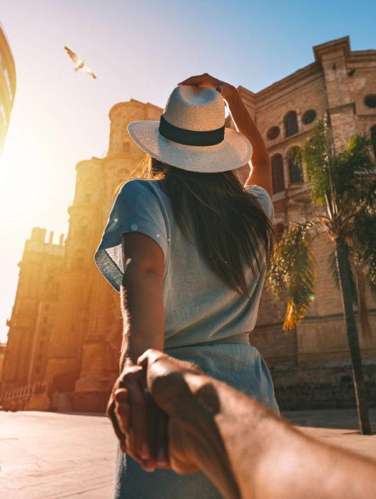 Mujer con sombrero junto a edificios antiguos bajo el sol.
