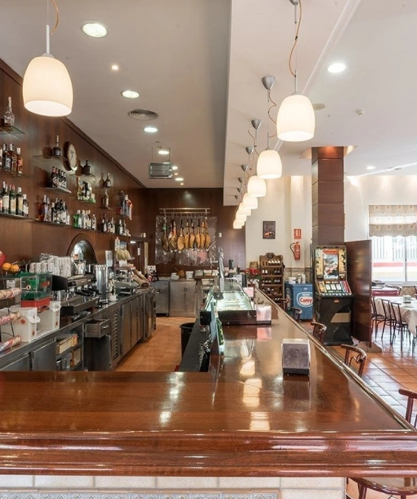 Bar restaurante con barra, vitrinas y luces colgantes en el interior
