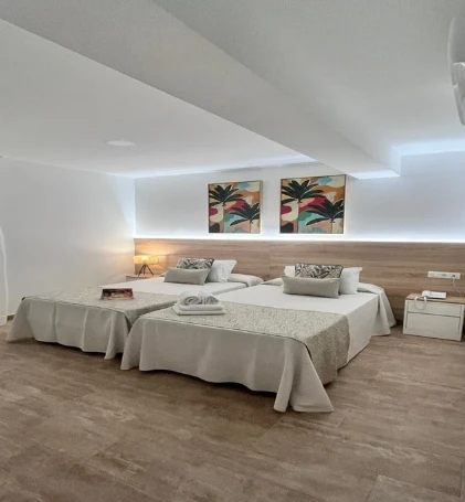 Sala con cuatro camas con ropa blanca y cuadros tropicales en la pared