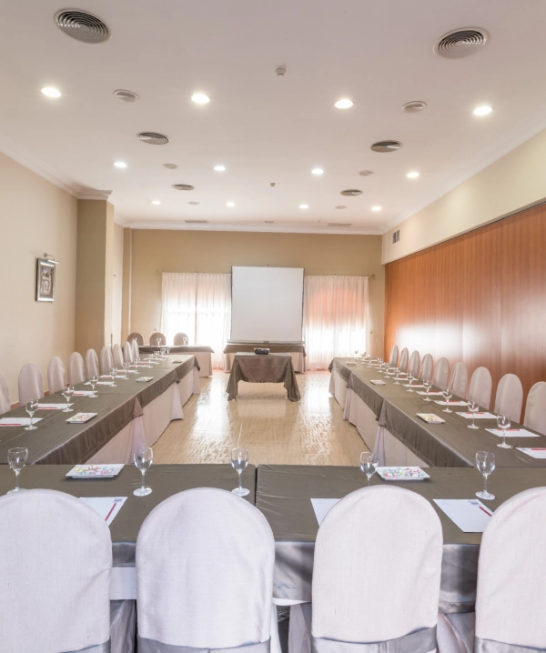 Sala de eventos con mesas servidas y sillas blancas, vista hacia proyector