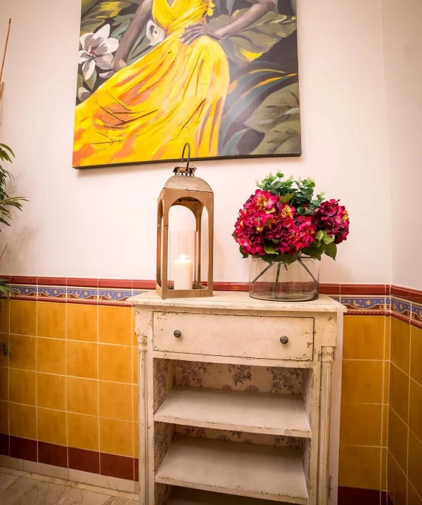 Velas en una l&aacute;mpara de bronce, flores rosas y obra de arte amarilla en pared