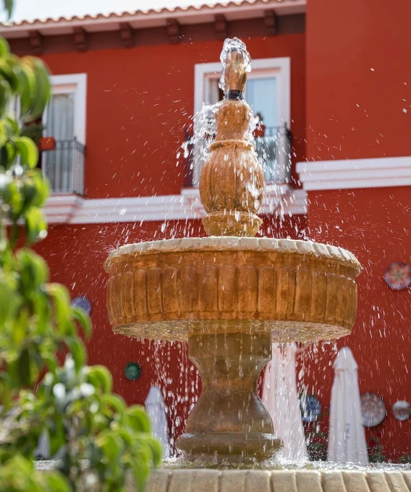 Fuente con chorro de agua y salpicaduras frente a pared roja del patio.