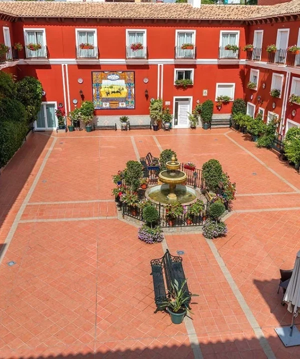 Patio interior con fuente circular y plantas, rodeado de habitaciones rojas.