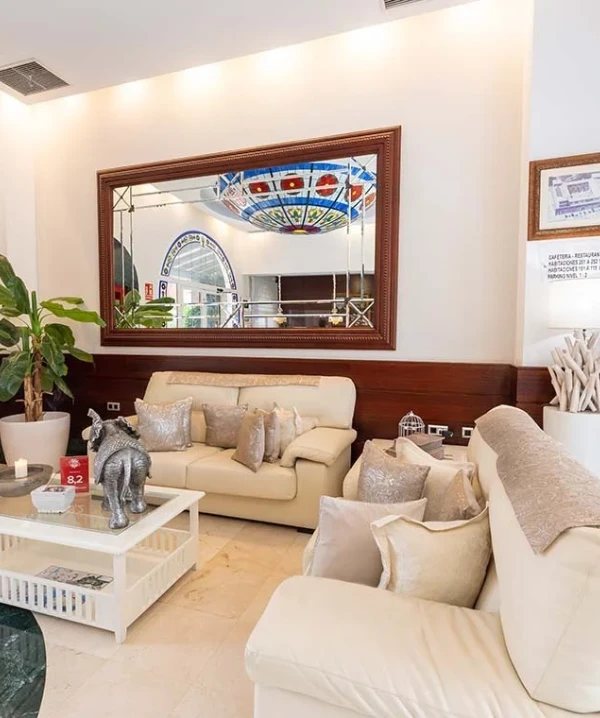 Sala de estar moderna con sof&aacute; beige, cojines y espejo decorativo.
