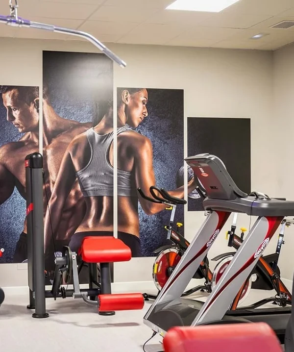 Cinta de correr en gimnasio con maniqu&iacute;es de fitness y posters en pared