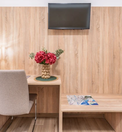 Sala con mesa de madera, florero con flores rojas y TV en pared.