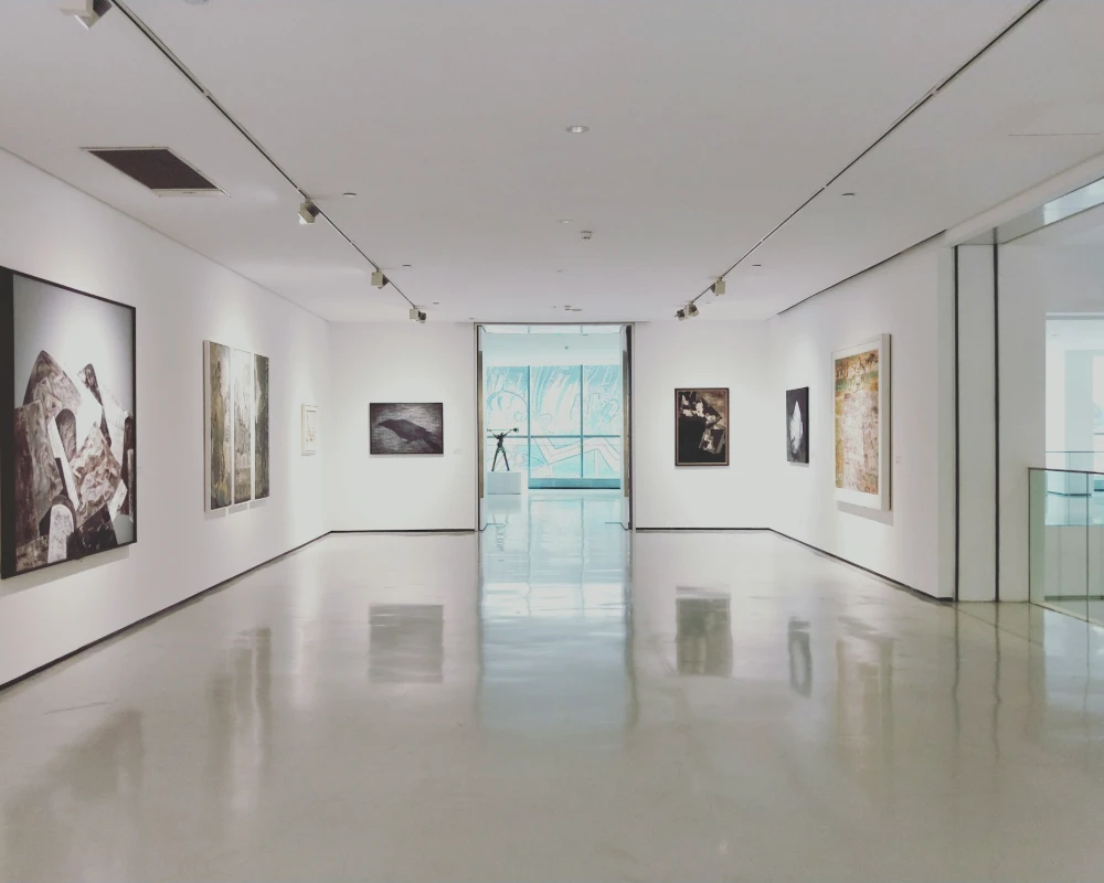 Galer&iacute;a de arte blanca con pinturas y suelo pulido, vista al fondo