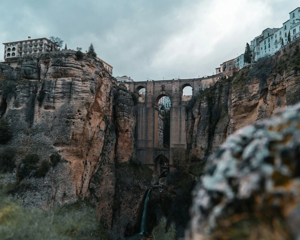 Acueducto de piedra sobre un ca&ntilde;&oacute;n con puentes de arcos y casas en la cima