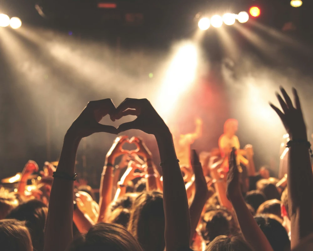 Manos formando un coraz&oacute;n en un concierto, con luces y p&uacute;blico al fondo