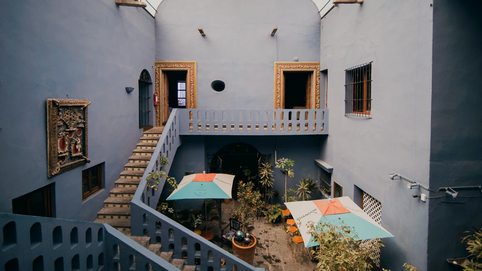 Patio con escalera y balc&oacute;n, sombrillas y cuadros en paredes blancas