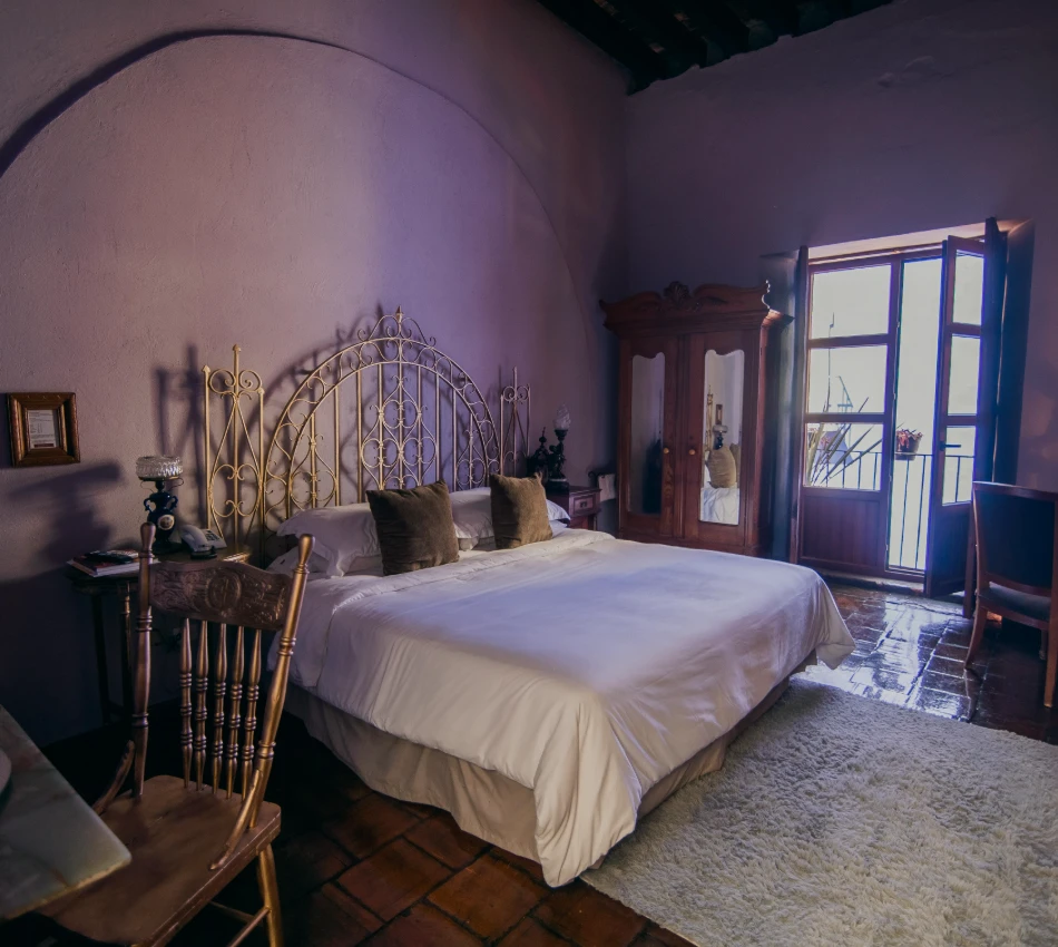 Dormitorio antiguo con cama de hierro, ventana azul y alfombra clara
