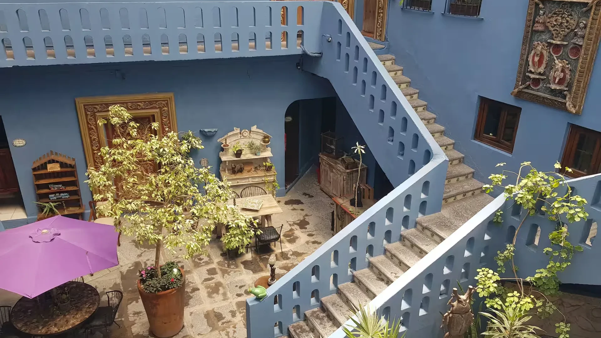 Patio azul con escaleras blancas, plantas y muebles decorativos, vista general