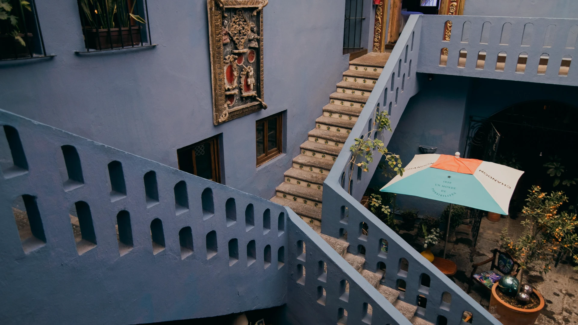 Patio con escaleras, barandilla azul y sombrilla bajo sol en un edificio antiguo