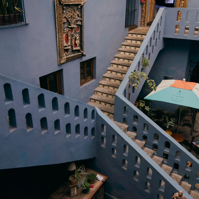 Patio con escalera y balcones azules, macetas y sombrilla naranja