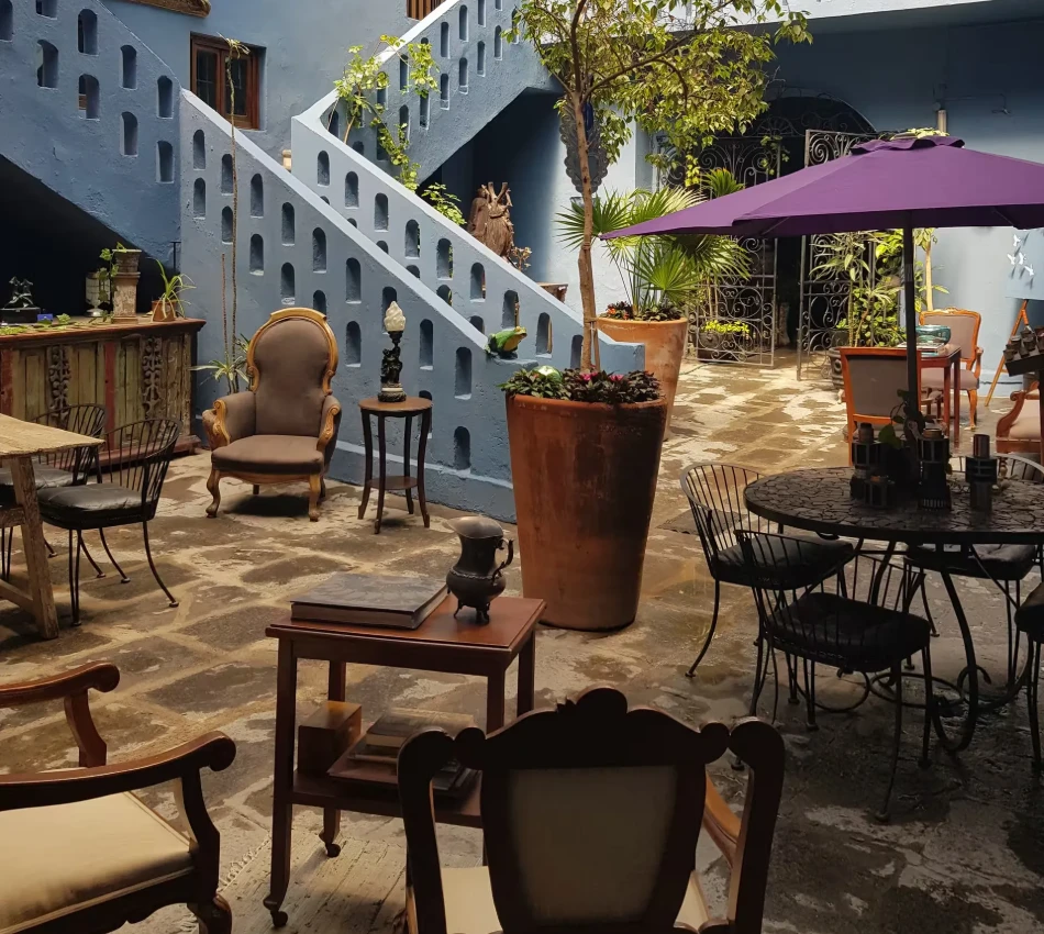 Patio con mesas, sillas y sombrilla morada junto a una pared azul con escalera de piedra