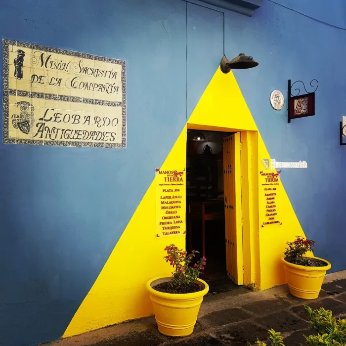 Entrada con tri&aacute;ngulo amarillo, macetas y letrero vintage en pared azul