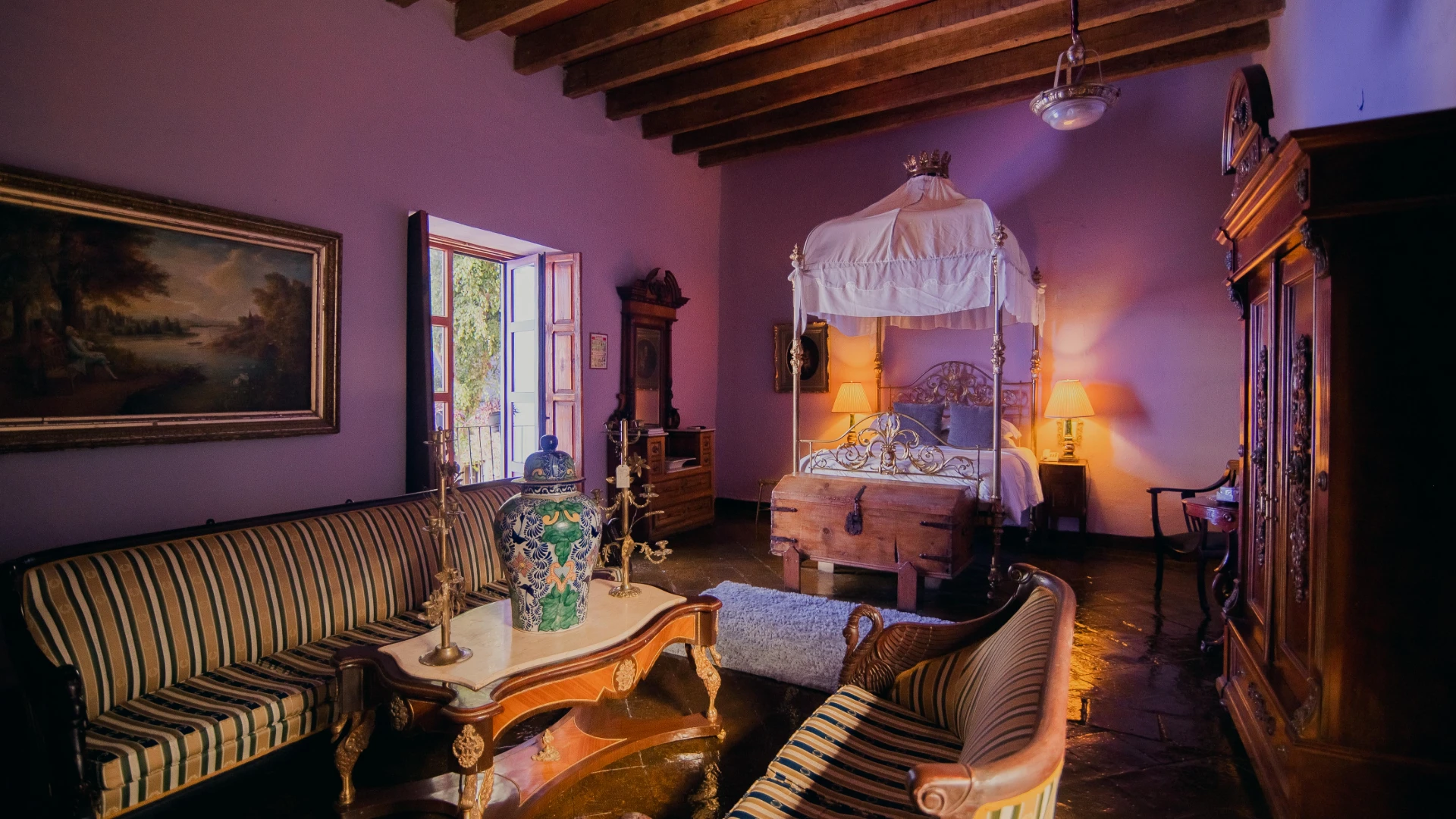 Dormitorio con cama con dosel, sillones y l&aacute;mparas encendidas, interior r&uacute;stico