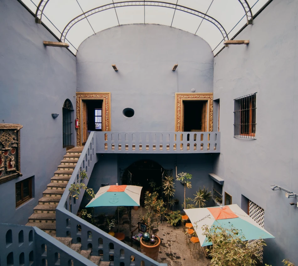 Patio interior con escaleras, balcones y sombrillas bajo un arco de cristal