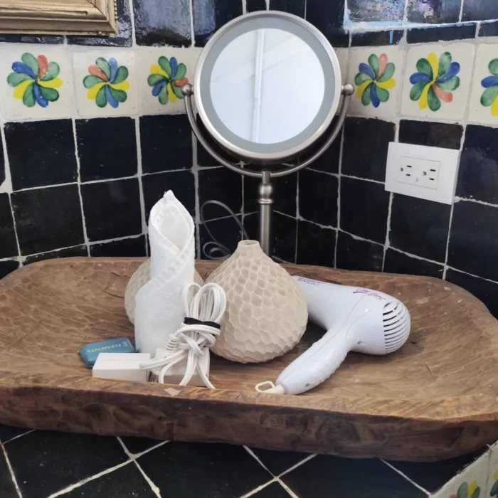 Secador y accesorios junto a espejo sobre mesa de madera en ba&ntilde;o decorado.
